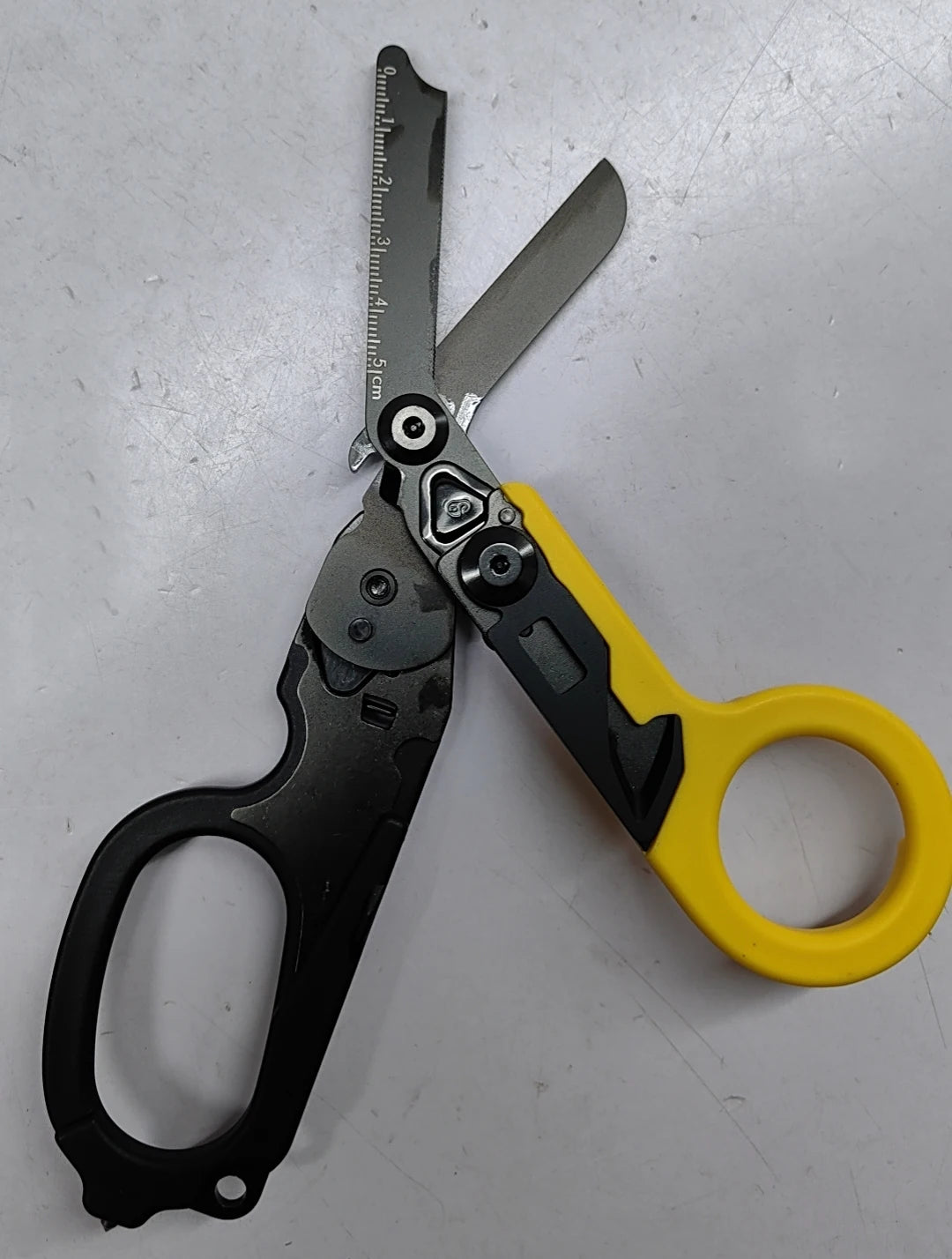 A pair of black and yellow tactical foldable shears with a measuring scale visible on the blade.