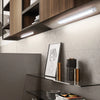 A modern kitchen cabinet with under-cabinet LED lighting illuminating a shelf displaying decorative cylindrical objects.