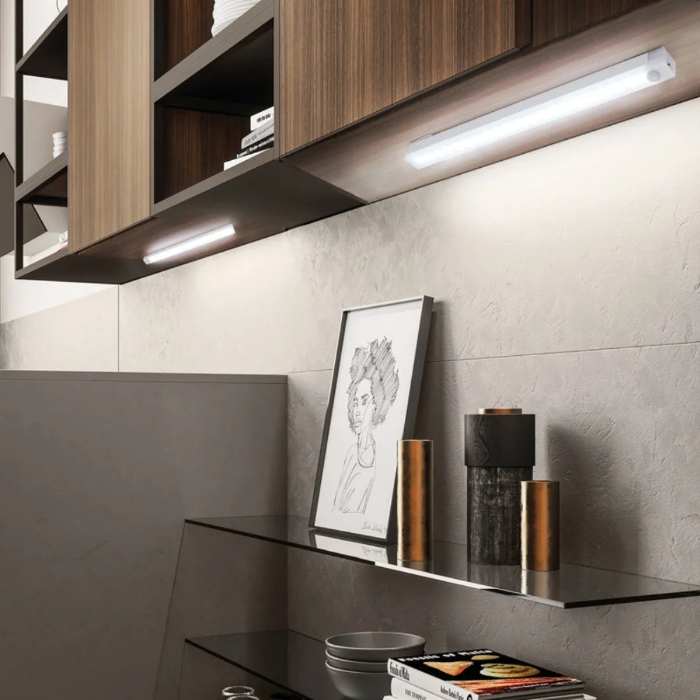 A modern kitchen cabinet with under-cabinet LED lighting illuminating a shelf displaying decorative cylindrical objects.