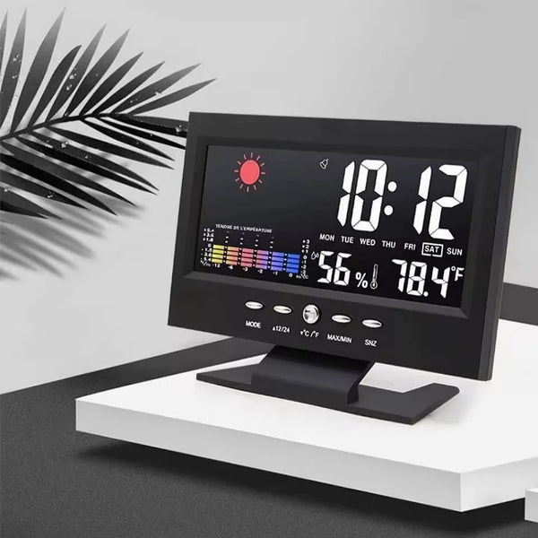 A black digital weather station clock displaying temperature, humidity, and time with a palm leaf silhouette in the backgroun