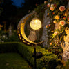 A solar moon light with an owl decoration hangs over a garden path at dusk.