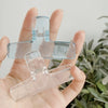 Eine Hand hält transparente Acryl-Federklammern vor einem unscharfen grünen Hintergrund.