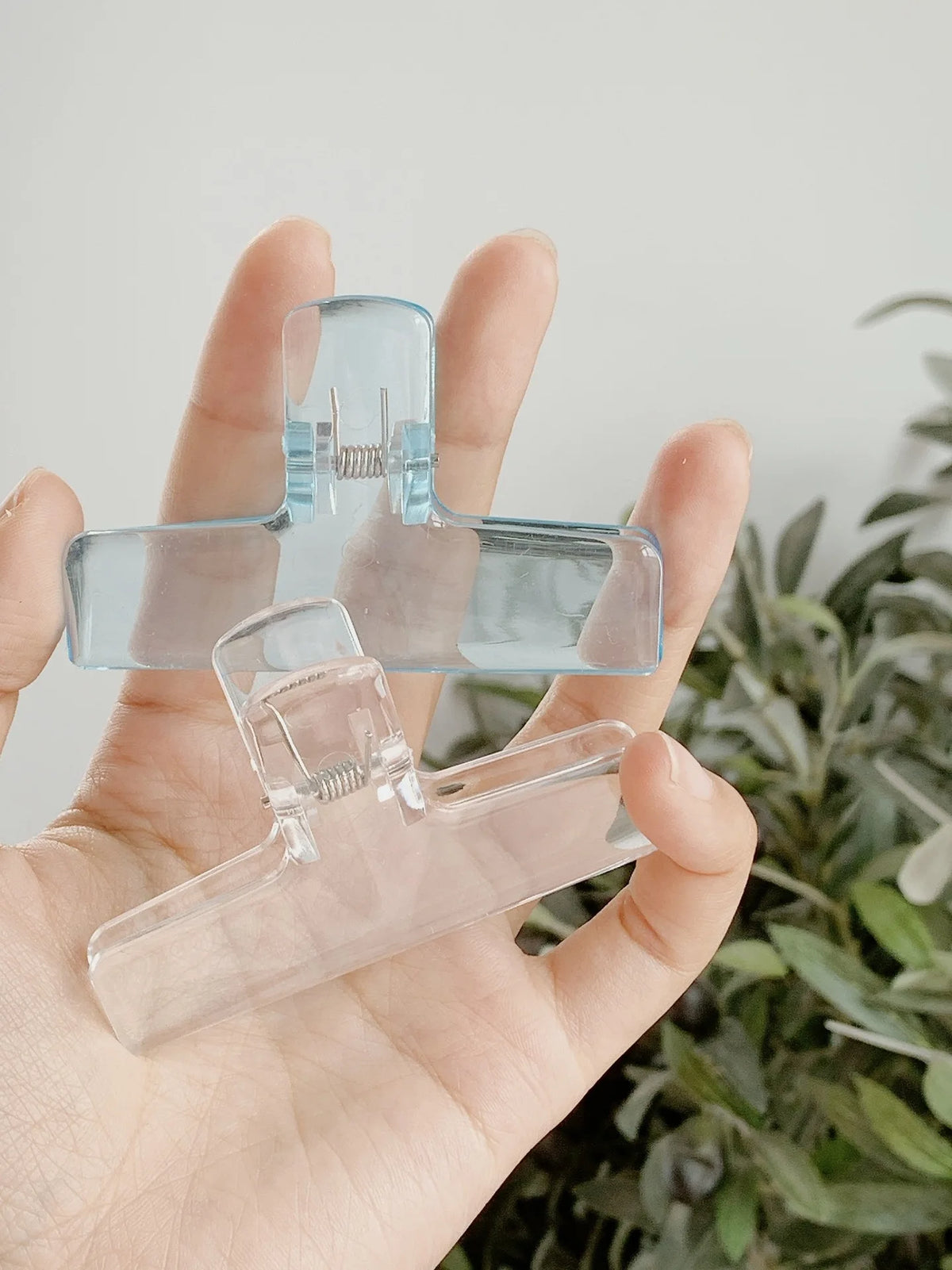 Eine Hand hält transparente Acryl-Federklammern vor einem unscharfen grünen Hintergrund.