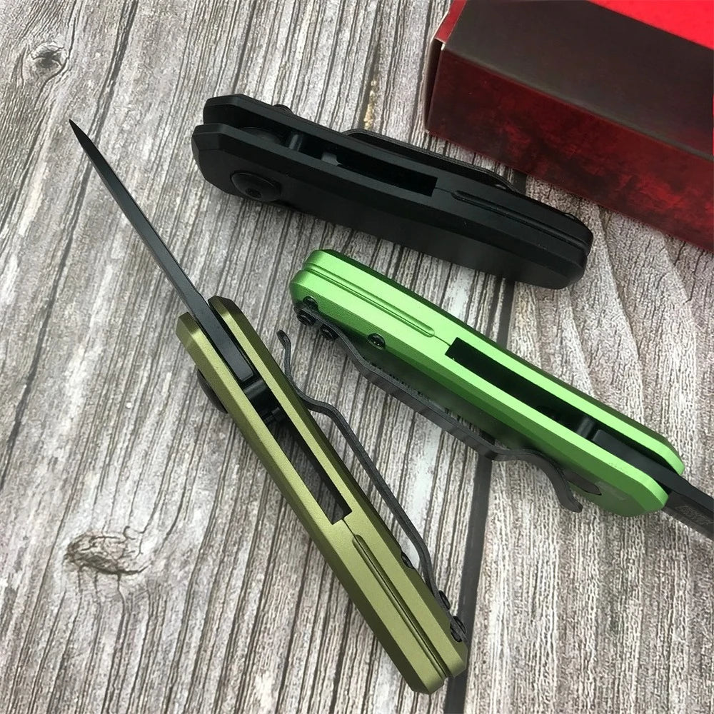A green compact folding pocket knife is shown next to a black knife and a red box on a wooden surface.