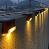 Row of warm yellow solar LED lights illuminating a textured concrete wall at dusk.