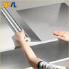 Une main décolle un autocollant de mur en aluminium adhésif d'une surface blanche.