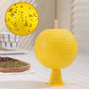 A bright yellow sticky fruit fly trap with a pink stick, next to a bowl of black seeds.