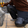 A person wearing dark clothing is adjusting black knee pads for construction or gardening work.