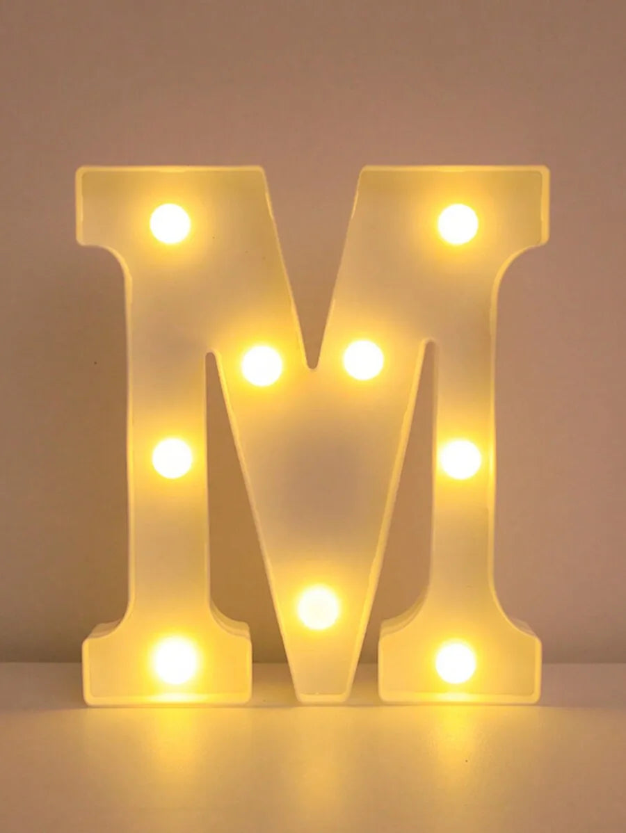 Luz nocturna de LED amarillo brillante en forma de M iluminando una superficie.