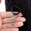 A silver camping buckle set with a black security lock is shown being held by a hand against a black fabric background.