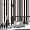 A modern bedroom featuring a black and white striped wallpaper, a dark light fixture, and a bed with gray bedding.