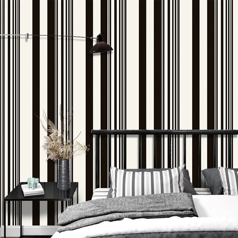A modern bedroom featuring a black and white striped wallpaper, a dark light fixture, and a bed with gray bedding.