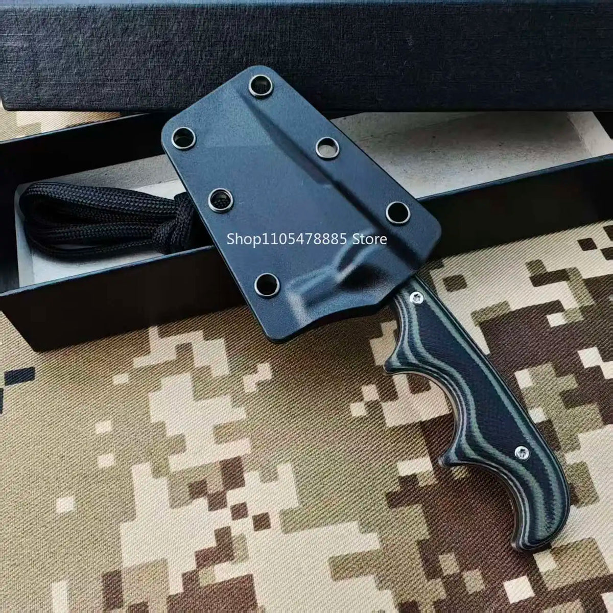 A dark blue compact fixed blade utility knife with a black sheath and a green patterned handle resting on a camouflage surfac
