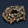 A strand of natural stone agate beads in shades of green and reddish-pink, laid out on a dark surface.