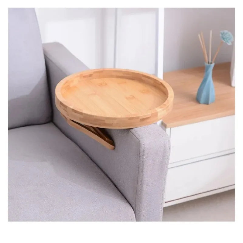 A round natural wooden tray is resting on the armrest of a gray sofa.