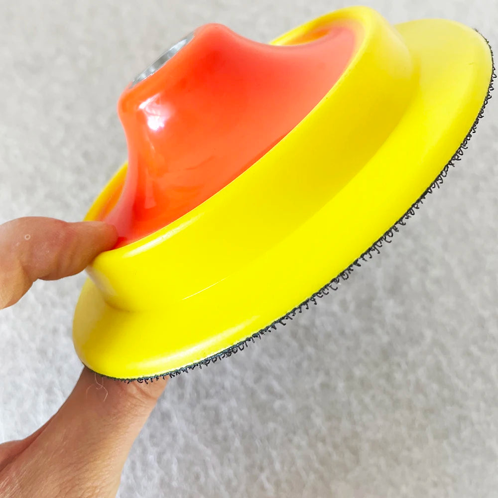 Eine Hand hält eine gelbe Rotationspolier-Pads mit einer orangefarbenen Finish-Oberfläche.