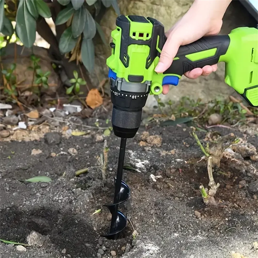 A hand holds a green garden auger with a black drill bit inserted into the soil.