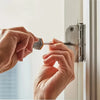 A person's hands are installing a wood screw into a door frame using a screwdriver.