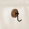 A round, dark wood wall hook with a black curved hanger mounted on a white wall.