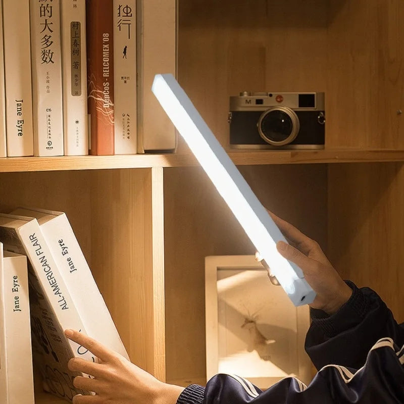 Eine Hand hält eine leuchtende weiße LED-Lichtleiste, die ein Buch auf einem Holzregal beleuchtet.