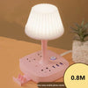 A pink multi-functional conversion desk lamp with USB and AC outlets sitting on a wooden surface.