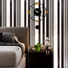 A modern living room interior featuring a dark sofa, vertical black and white striped walls, and a minimalist wall clock.