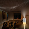 A white Galaxy Star Projector night light illuminates a room with a dark, starry ceiling and a tiger-print blanket.