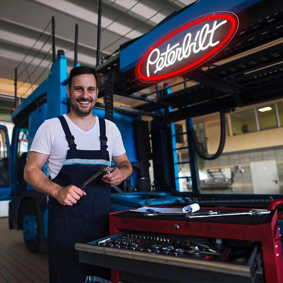 A man in overalls stands next to a red grill, with an acrylic neon wall sign visible above.