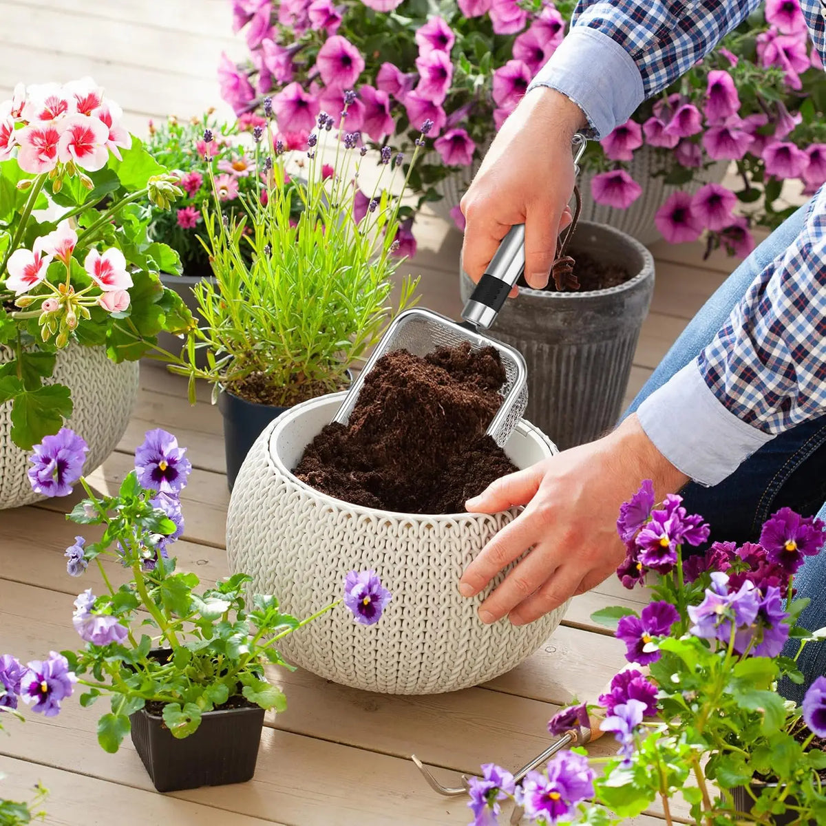 A hand is using a heavy duty stainless steel soil sieve set to pour dark potting soil into a woven plant pot.