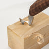 A hand holding a small metal carving tool on a wooden block, demonstrating a precision wood carving kit.