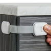 A hand is using an adjustable child safety lock to open a cabinet door.