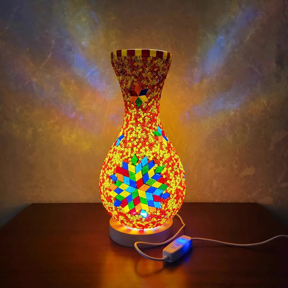 Lámpara de mesa de vidrio entrelazado y colorido con diseño vibrante, iluminada contra un fondo oscuro.