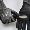 A hand wearing black anti-cut work gloves is holding a silver utility knife.