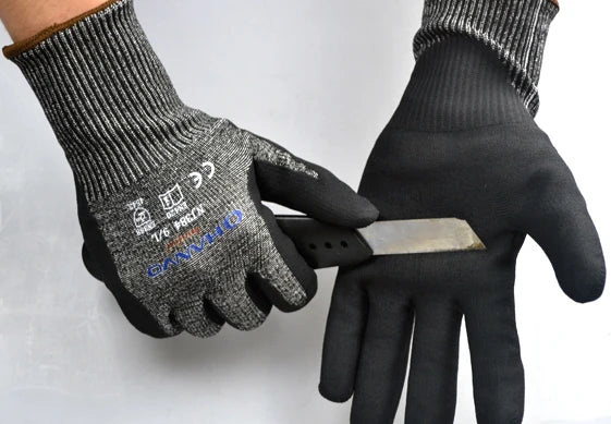 A hand wearing black anti-cut work gloves is holding a silver utility knife.