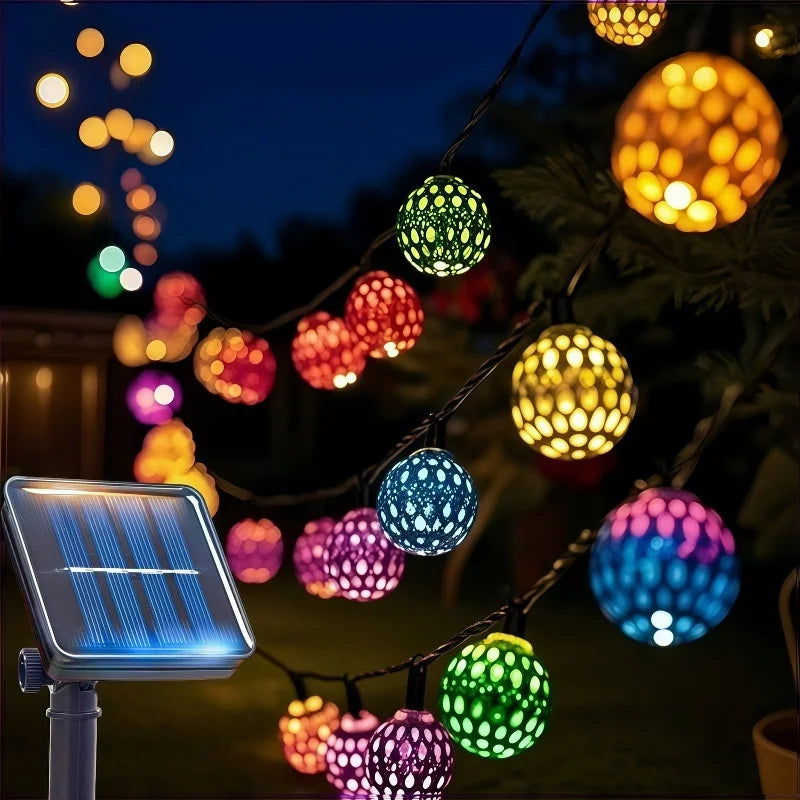 Luces de cuerda marroquíes con orbes LED coloridos colgados en una rama oscura de árbol por la noche