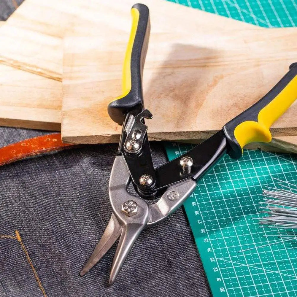 A pair of black and yellow heavy duty aviation tin snips shears resting on a wooden cutting board and a green grid mat.