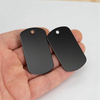 Two black aluminum metal stamping tags are held in a hand against a white background.