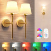 A pair of modern brass wall sconces with white shades and remote controls mounted on a textured wall.