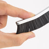 A hand holds a black grout gap cleaning brush set, showing the bristles and metal frame.