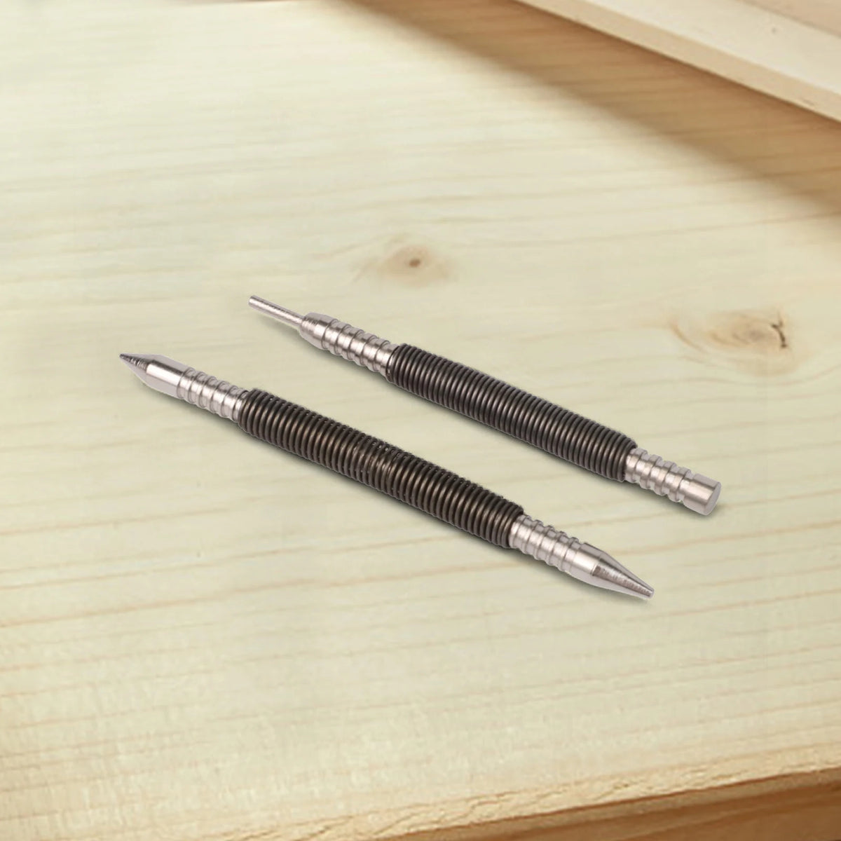 A pair of silver dual-head spring nails lying on a light wooden surface.