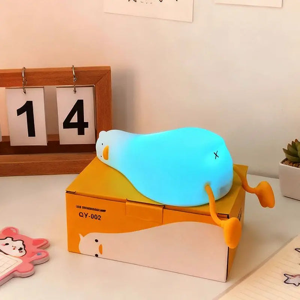 A glowing blue silicone duck night light rests on an orange box.
