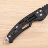 Black folding keychain knife with a textured handle and silver accents resting on a light wooden surface.