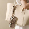 A beige leather handbag with a tan strap and a matching eyeglass case hanging from it.