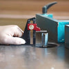 A hand holds a precision depth gauge against a piece of wood on a workbench.