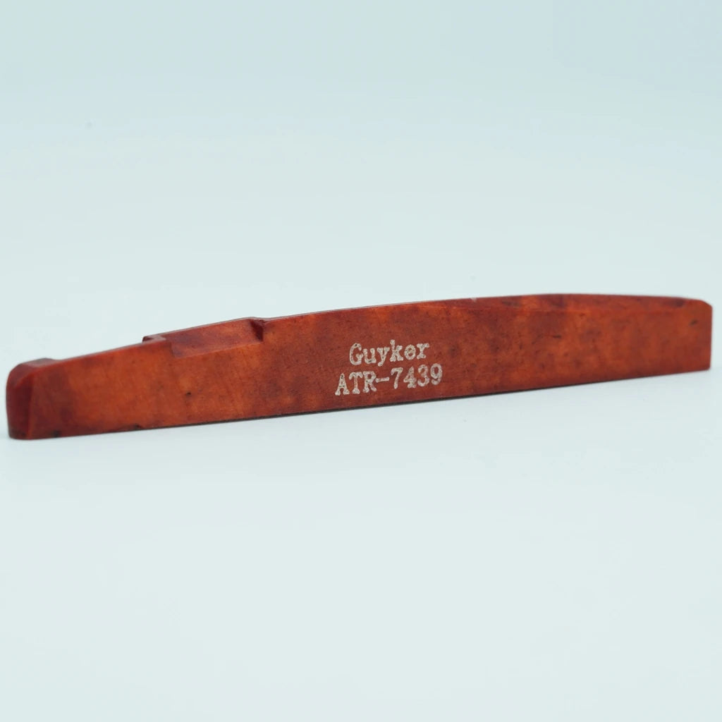 A wooden guitar bone bridge saddle labeled Guyker ATR-7439