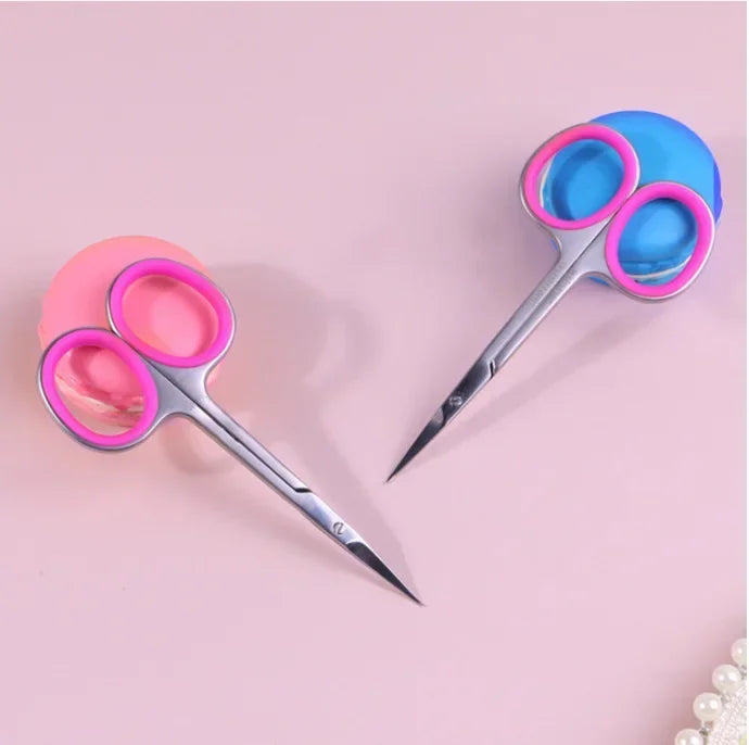 A pair of professional stainless steel nail cuticle trimmers with pink and blue handles are shown on a light pink background.