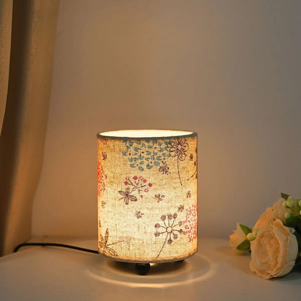 A minimalist USB desk lamp with a cylindrical fabric shade featuring a floral print, resting on a white surface.