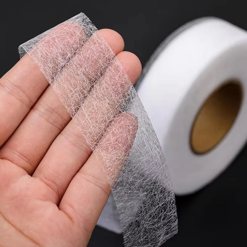 A hand holds a roll of clear, sheer iron-on hemming tape for fabric edging.
