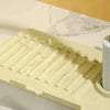 A yellow silicone drain mat with a manifold design is shown draining water into a sink.