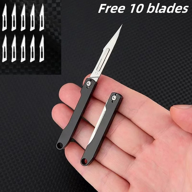 A hand holds a black mini folding art knife with a silver blade, next to ten spare blades.